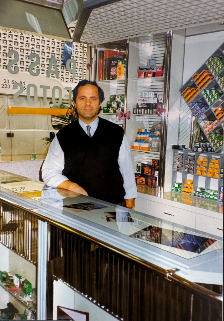 Der Gründer von Fotowest hinter der Ladentheke, im Schaufenster der Schriftzug Passfotos